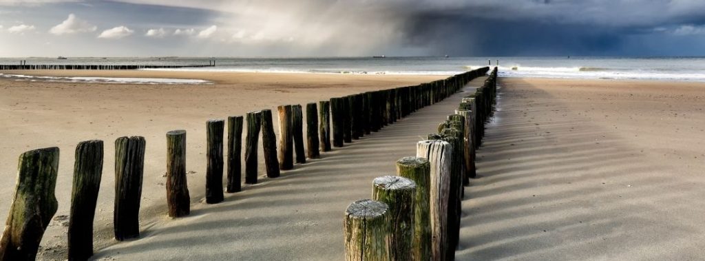 Strand mit Holzpfählen und Wolkenhimmel